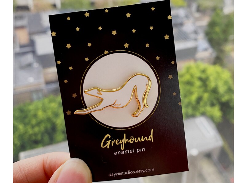 Pode incluir: Pin de esmalte dourado de um galgo em um cart&atilde;o preto com estrelas douradas. O cart&atilde;o diz "Greyhound enamel pin" e "dayzistudios.etsy.com".