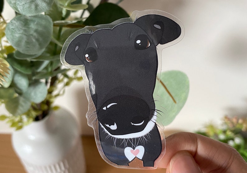 May include: A black and white cartoon dog sticker with a pink heart on its chest. The dog has a white collar and is looking at the camera.