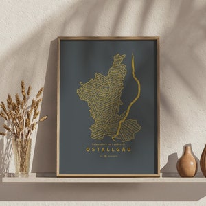 May include: A framed print of a map of Ostallgäu, Germany, with the names of the municipalities in gold lettering on a dark grey background.