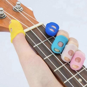 May include: A set of four finger picks for playing guitar or ukulele. The picks are made of silicone and come in yellow, blue, light blue, and pink.