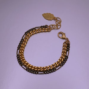 Pode incluir: Um bracelete de corrente dourada com um design de corrente dupla. Uma corrente é uma corrente grossa de elos e a outra é uma corrente mais fina e delicada. O bracelete tem um fecho em forma de folha.