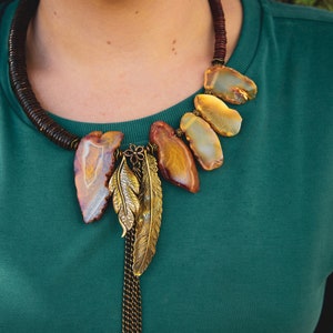 May include: A brown leather necklace with a large agate pendant and two gold feather charms. The agate is a mix of brown, orange, and white.