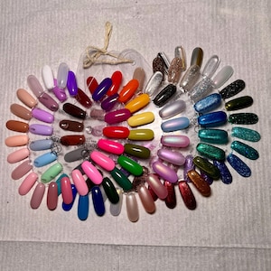 Puede incluir: Un muestrario de colores de esmalte de uñas de plástico transparente con una variedad de colores. El muestrario tiene forma de calabaza y tiene una cuerda para colgar. Los colores incluyen tonos de rosa, rojo, azul, verde y brillo.