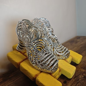 Op de afbeelding: Een paar zilveren schoenen met hoge hakken met een uitgesneden kooiontwerp, een metallic afwerking en overal ingebedde heldere strass-steentjes. De schoenen hebben een ronde neus en een gebogen hak met een gedetailleerd, gelaagd patroon.
