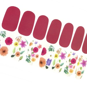 May include: Nail polish wraps with a floral design. The wraps are white with pink, purple, and yellow flowers. The wraps are paired with solid red nail polish wraps.