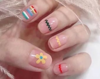 May include: Close-up of a hand with five fingernails painted with different designs. The nails are painted with a light pink base and have various colorful designs, including stripes, zigzags, a flower, and a wavy line.