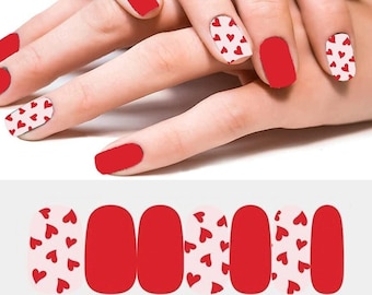 May include: Red nail polish and nail wraps with a heart pattern. The nail wraps alternate between solid red and a light pink background with small red hearts. The image shows the nail wraps and a hand with the nail wraps applied.