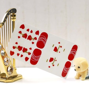 May include: A sheet of red and white nail art stickers with a heart design and the text "Love you". The stickers are on a white background and are next to a gold harp.