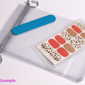 May include: A clear plastic bag containing a set of leopard print nail wraps and a blue nail file. The nail wraps are on a white card with a gold glitter accent. The bag is tied with a silver ribbon.