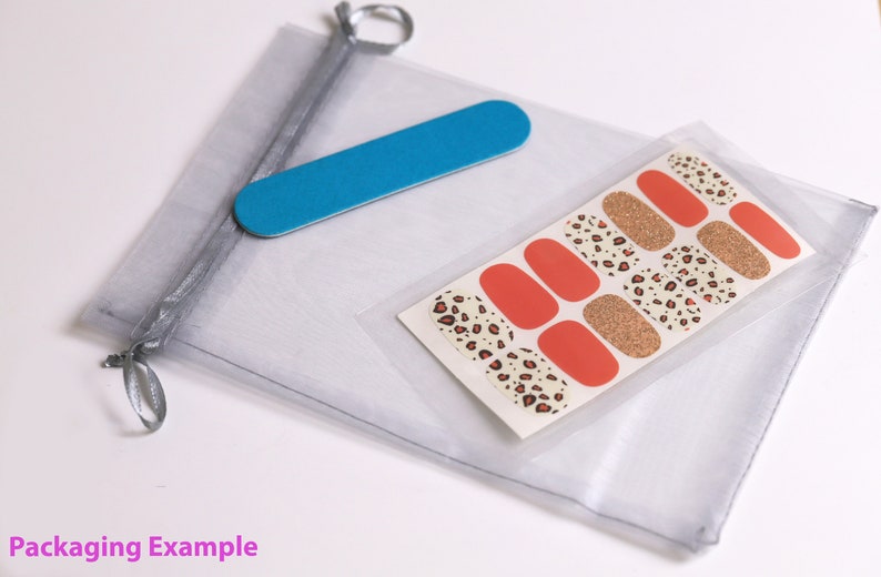 May include: A clear plastic bag containing a set of leopard print nail wraps and a blue nail file. The nail wraps are on a white card with a gold glitter accent. The bag is tied with a silver ribbon.