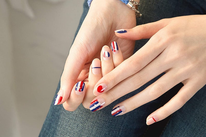 May include: Close-up of hands with red, white, and blue nail polish. The nails are painted with stripes and dots.