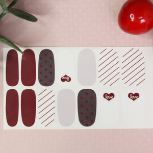 May include: A sheet of nail polish wraps with a variety of designs, including solid red, polka dots, stripes, and a white base with the word "love" in a heart shape.