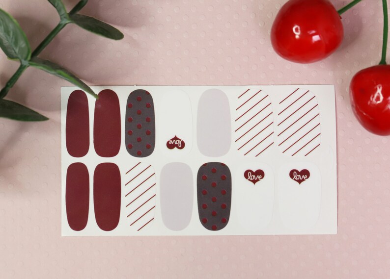 May include: A sheet of nail polish wraps with a variety of designs, including solid red, polka dots, stripes, and a white base with the word "love" in a heart shape.
