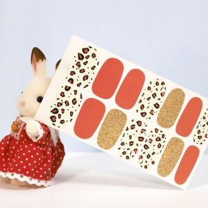May include: Nail art stickers featuring a mix of designs. The sheet includes solid orange, gold glitter, and leopard print patterns in black and red. The stickers are displayed against a light blue background.