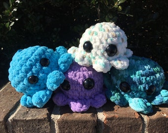Può includere: Quattro peluche di polpo all'uncinetto in diversi colori: blu, viola, verde e bianco con macchie marroni. Ogni peluche ha grandi occhi neri.