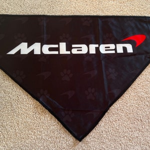 Op de afbeelding: Zwarte driehoekige bandana met een wit "McLaren" logo en een rode swoosh. De bandana heeft een herhalend patroon van poot afdrukken.