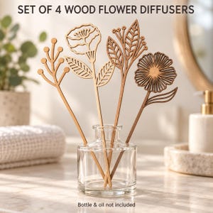 May include: A set of four wood flower diffusers featuring laser-cut floral and botanical designs on thin stems. The set includes a branch-like form, a poppy-style flower, a leafy stalk, and a daisy-like bloom. Text reads: SET OF 4 WOOD FLOWER DIFFUSERS.