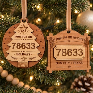 May include: Two wooden Christmas ornaments hanging by tan ribbons. The left circular ornament features a tree shape with the text HOME FOR THE HOLIDAYS and 78633. The right rectangular ornament displays the text HOME FOR THE HOLIDAYS, 78633, and SUN CITY TEXAS.