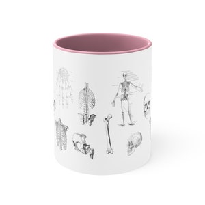 May include: White ceramic mug with a pink interior. The mug features a black and white anatomical illustration of a human skeleton with various bones and the skull.