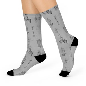 May include: A pair of gray socks with a black anatomical skeletal pattern. The socks are shown on a model's feet.