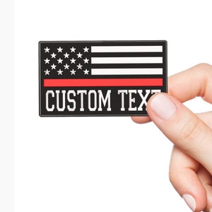 May include: A rectangular patch featuring the American flag design with a red stripe and the words "CUSTOM TEXT" in white. The patch is black, white, and red.