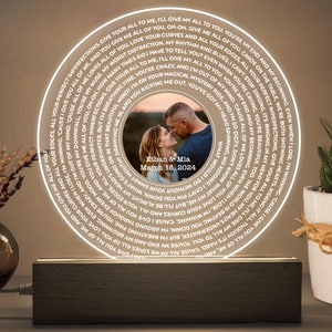 May include: A white LED night light with a circular design. The light features a couple's photo in the center and a swirling text pattern around the photo. The text reads "Give your all to me, I'll give my all to you. You're my end and my beginning. Even when I lose, I'm winning 'cause I give you all of me, and you give me all of you." The text also includes the couple's names and wedding date: "Ethan & Mia, March 15, 2024".