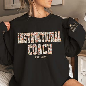 May include: Black sweatshirt with a floral design that says "Instructional Coach" and "Est. 2025" in gold lettering.