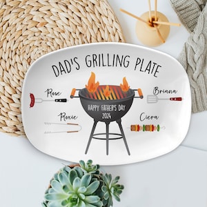 May include: White oval serving platter with the text "Dad's Grilling Plate" and a cartoon illustration of a grill with flames, a spatula, tongs, and skewers. The text "Happy Father's Day 2024" is printed below the grill. The names "Rose", "Roxie", "Briana", and "Ciera" are printed around the grill.