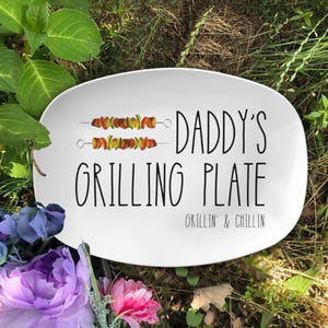 May include: White oval serving platter with the text "Daddy's Grilling Plate" and "Grillin' & Chillin'" in black. Two skewers of grilled vegetables are pictured above the text.
