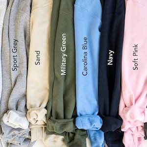 May include: A selection of ten folded sweatshirts in various colours, including white, ash, sport grey, sand, military green, carolina blue, navy, soft pink, dark heather, and black.