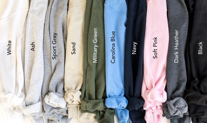May include: A selection of ten folded sweatshirts in various colours, including white, ash, sport grey, sand, military green, carolina blue, navy, soft pink, dark heather, and black.