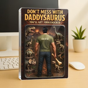 May include: A humorous illustration of a man with the name "DAVID" on his shirt standing in front of a group of dinosaurs. The text reads "Don't mess with Daddysaurus You'll get Jurassic-kicked".