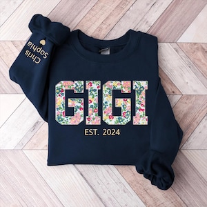 May include: Navy blue sweatshirt with a floral print that spells out "GIGI" and the text "EST. 2024" below.