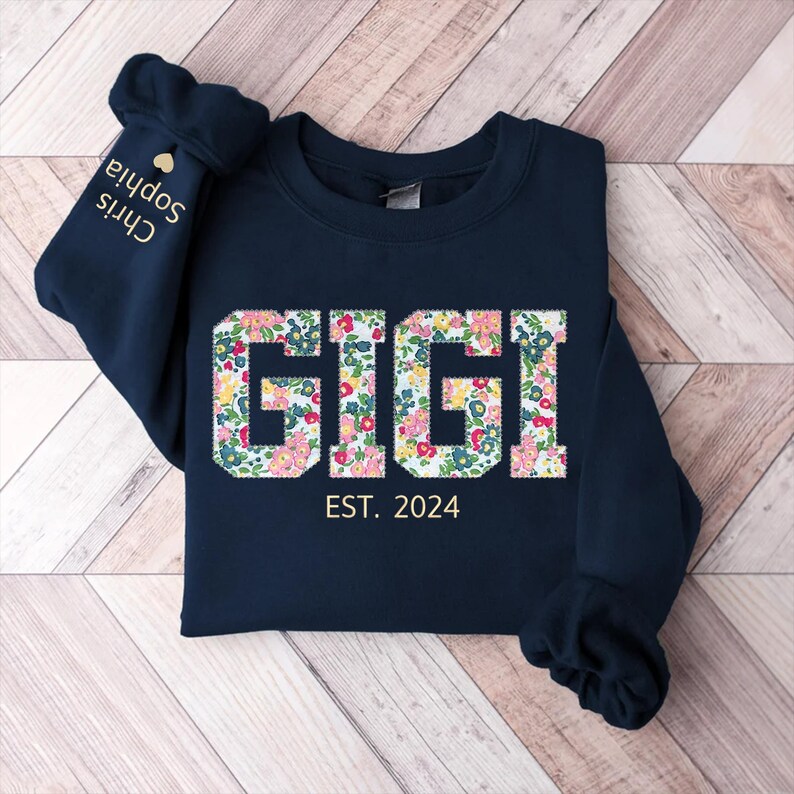 May include: Navy blue sweatshirt with a floral print that spells out "GIGI" and the text "EST. 2024" below.