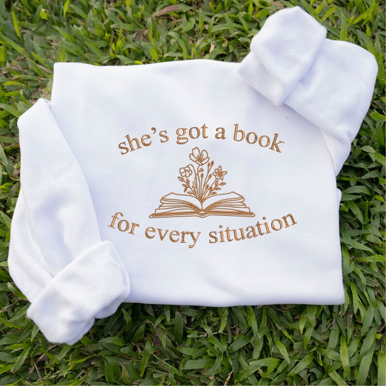 May include: White baby onesie with brown embroidery that reads "she's got a book for every situation" with a stylised image of a book with flowers on top.