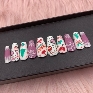 May include: A set of false nails with a Christmas theme. The nails display various designs, such as snowflakes, Christmas trees, and the text "MERRY CHRISTMAS". The colour scheme includes white, purple, green, and red, creating a festive appearance.