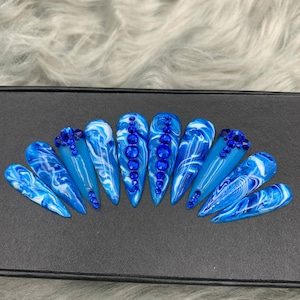 May include: Set of ten blue and white swirl patterned stiletto false nails with blue rhinestones.