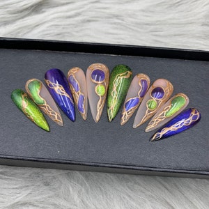 May include: Set of ten false nails with a green, blue, and gold design. The nails are long and pointed, and they have a glossy finish.