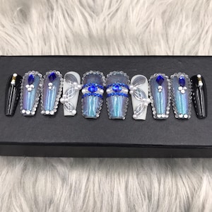 May include: Set of ten blue and silver iridescent coffin-shaped press-on nails with white pearl and blue rhinestone accents.