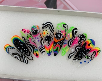 Puede incluir: Conjunto de diez uñas postizas con base blanca y diseños abstractos coloridos. Los diseños incluyen remolinos, ojos e arcoíris.