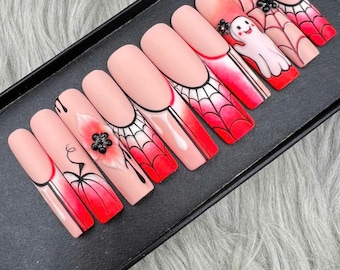 May include: A set of ten artificial nails with a Halloween theme. The nails are painted with a light pink base and feature designs including spiderwebs, a ghost, and a flower. The tips are red, and some nails have black embellishments.