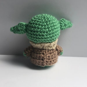 May include: A crocheted green and brown plush toy resembling a popular fictional character. The toy has large ears and a small body.