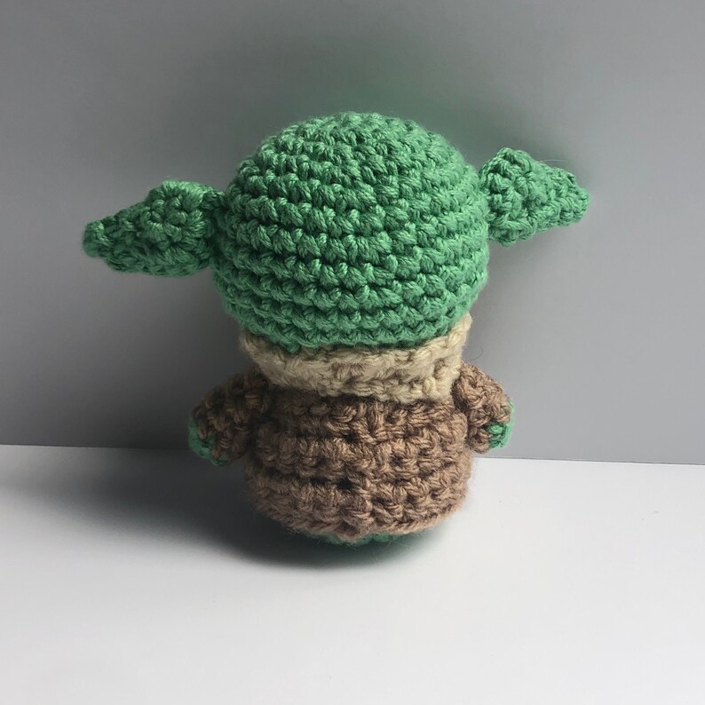 May include: A crocheted green and brown plush toy resembling a popular fictional character. The toy has large ears and a small body.