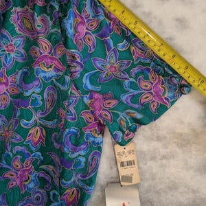 May include: A short-sleeved top with a vibrant floral and paisley pattern in shades of teal, purple, and blue. The fabric is measured with a yellow tape measure. A price tag is attached. The top has a gathered neckline and sleeves.