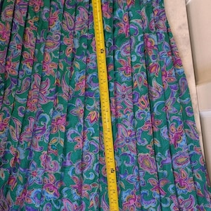May include: A long, pleated skirt with a vibrant floral pattern in shades of green, purple, and blue. A yellow measuring tape shows the skirt's length. The skirt's length is approximately 76 cm.