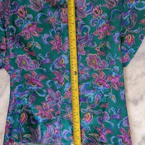 May include: A green blazer featuring a floral design in purple, pink, and blue. A yellow tape measure shows the blazer's length to be approximately 56 cm.