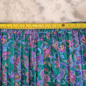 May include: A green skirt with a floral paisley pattern in shades of purple, blue, and pink. The skirt measures approximately 43 cm across the top, as measured by a yellow tape measure.