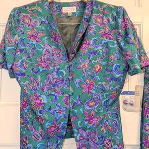 May include: A vintage green two-piece suit with a floral paisley pattern in purple, blue, and yellow. The jacket has short sleeves and a button-up front. The label reads "Papell".