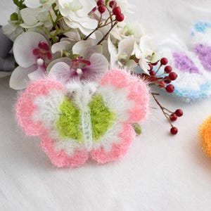 May include: Three crocheted butterfly ornaments in pink, blue and orange. The butterflies are made with fluffy yarn and have a white centre.