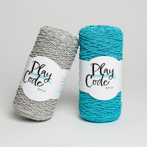 Op de afbeelding: Twee spoelen Play Code garen, één grijs en één turquoise, worden getoond tegen een witte achtergrond. Elke spoel heeft een wit etiket met de woorden "Play Code" in een scriptlettertype. Het garen is strak gewikkeld en de etiketten bevatten Koreaanse tekst.